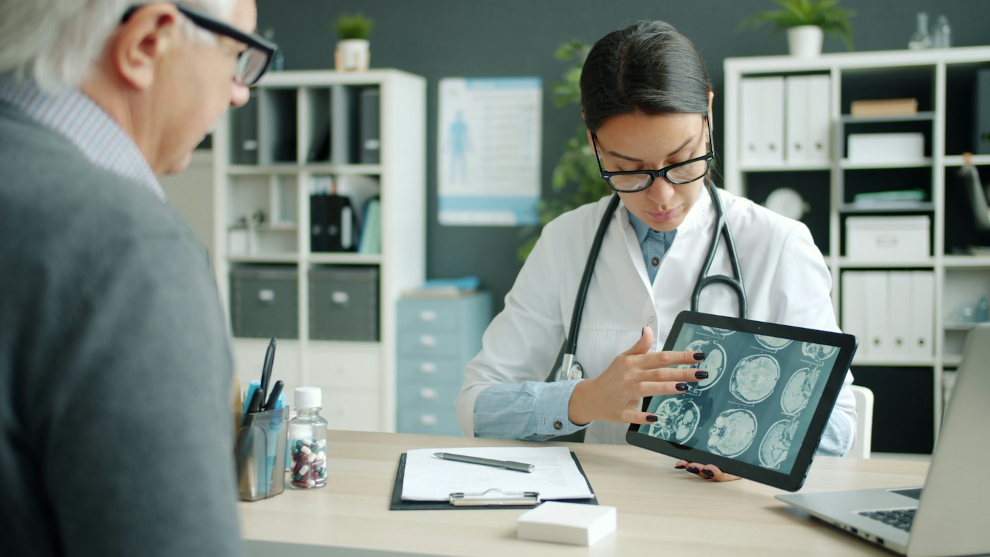 Arzt erklärt einem Patienten medizinische Scans auf einem Tablet.